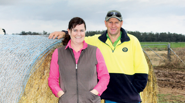 A man and woman standing in front of bale of hay