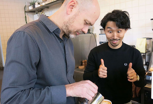 Man making thumbs up sign watching milk being poured into coffee