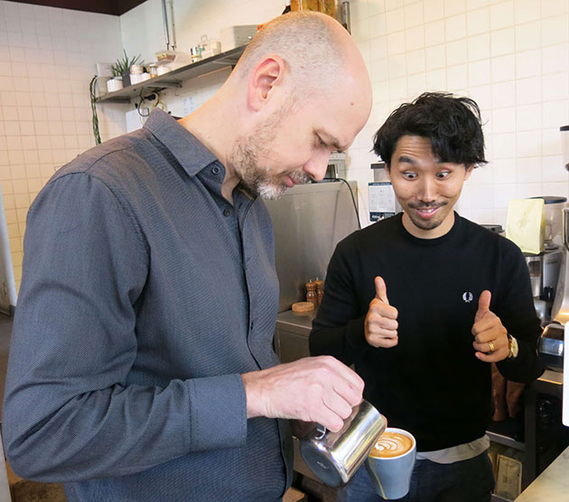 Man making thumbs up sign watching milk being poured into coffee