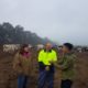 Three people chatting on a farm in front of cows