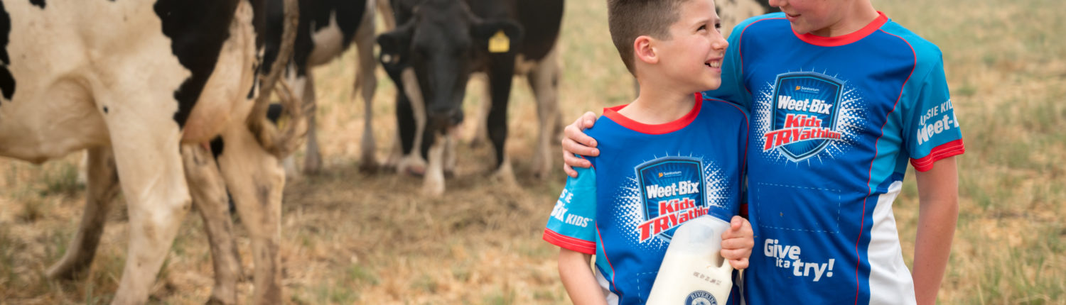 Two children standing in front of cows holding Riverina Fresh milk wearing Weet-Bix shirts