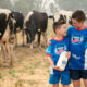Two children standing in front of cows holding Riverina Fresh milk wearing Weet-Bix shirts