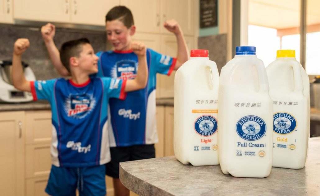 Two boys smiling and flexing arms behind Riverina Fresh milk